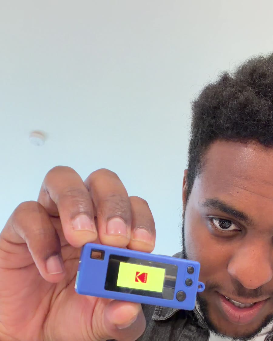 Zazi holding the tiny blue Kodak Charmera camera up to the lens with his own face on its screen